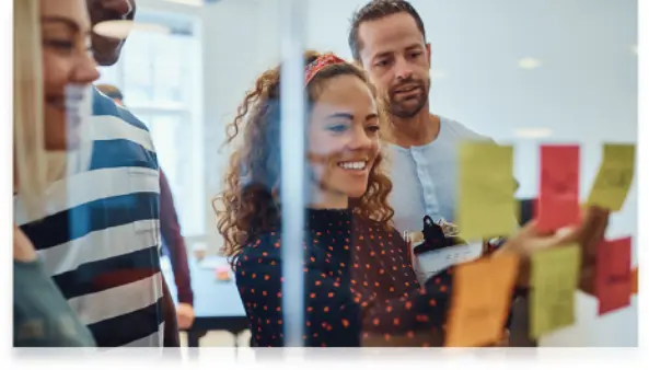 Team of colleagues collaborating with sticky notes on a glass wall during a brainstorming session.