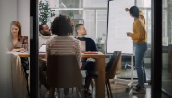 Team collaborating in an office as a presenter explains ideas on a whiteboard during a meeting.